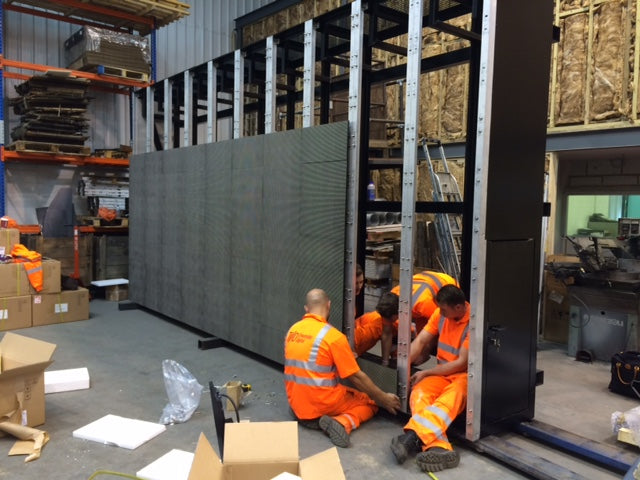 Three men installing an Ultravision LED Digital Display on a frame in a warehouse.