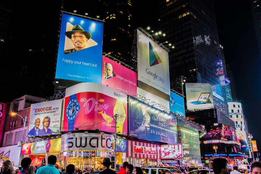 Digital and static billboards lit up at night, being viewed by a large crowd.